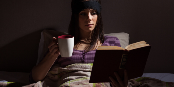 Woman reading and drinking cofee instead of sleeping on the bed
